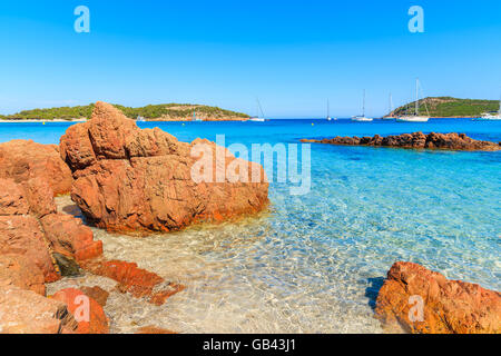 Rote Farbe Felsen am Strand von Santa Giulia mit azurblauen Meerwasser, Korsika, Frankreich Stockfoto