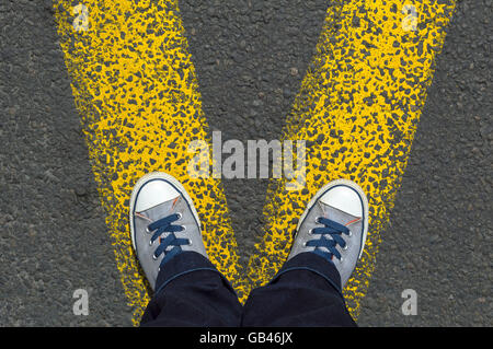 Turnschuhe stehen mit der gelben Straße Markierungslinien auf Asphaltdecke. Stockfoto