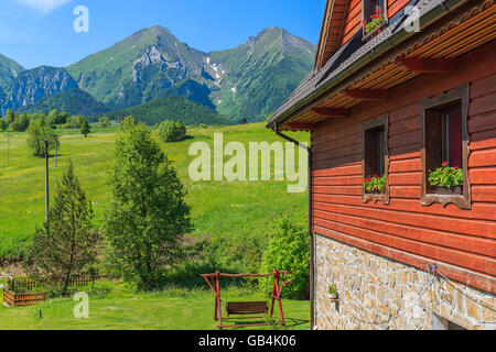 Holzhaus auf der grünen Wiese mit Tatry Bielskie Berge im Hintergrund im Sommer, Slowakei