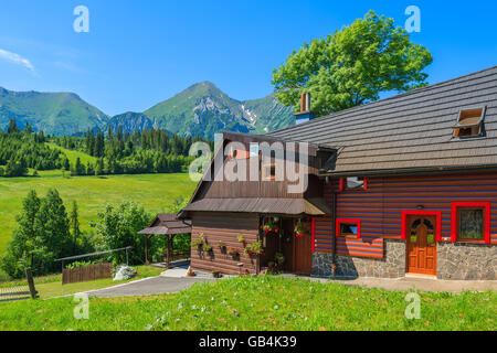Typisches Holzhaus auf grüner Wiese mit Tatry Bielskie Bergen im Hintergrund im Sommer, Slowakei