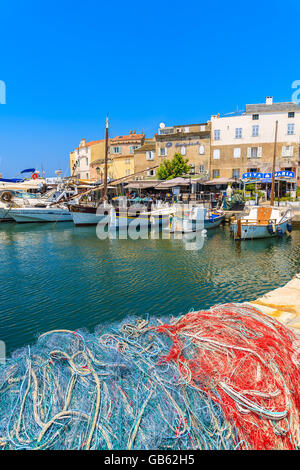 SAINT FLORENT, Korsika - 30. Juni 2015: Fischernetze im Vordergrund mit Booten in Ferne im kleinen Hafen von Saint Florent, Stockfoto