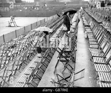 Ein paar Zuschauer mit Regenschirmen halten an und trotzen dem Regen, der bei den britischen Hartplatz-Tennismeisterschaften in Bournemouth nicht mehr gespielt hatte. Stockfoto