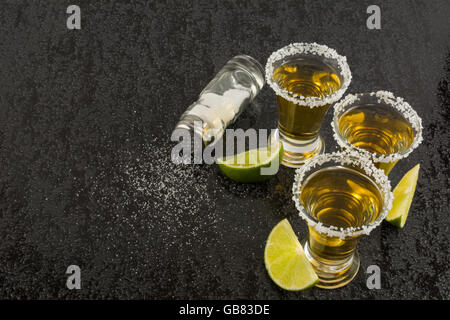 Tequila Shots mit Kalk und Salz auf schwarzen Tisch. Tequila.  Mexikanische Tequila Gold Stockfoto