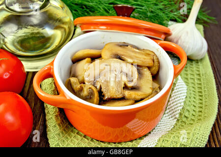 Champignons gebraten in einer roten Keramiktopf auf eine Serviette, Knoblauch, Dill und Pomidoryna Hintergrund dunkle Holzbretter Stockfoto