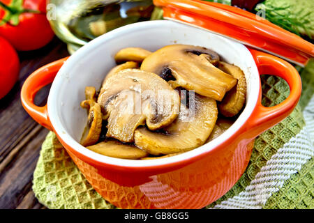 Champignons gebraten in einer roten Keramiktopf auf eine Serviette, Knoblauch, Dill und Pomidoryna Hintergrund Holzbrett Stockfoto