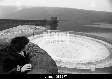 Ein Besucher des Ladybower Reservoir in der Nähe von Bamford, Derbyshire, das bis zum Rand von starken Regenfällen gefüllt wurde, erlebt Tausende von Gallonen Wasser, die durch ein riesiges "Steckloch" mit einem Durchmesser von 50 Fuß freigesetzt werden. Stockfoto