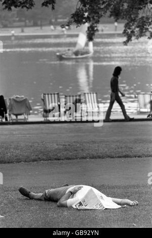 Ein Mann, der unter einer Zeitung in der Nähe des Serpentine im Hyde Park, London, sonnenbaden geht. Stockfoto