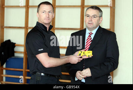 Ratsherr Alan Campbell, rechts, wird von einem Offizier während einer Fotozelle im Polizeihauptquarter in Ponteland eine Taserpistole gezeigt. Stockfoto