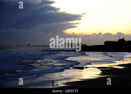 Sturmwolken ziehen über die Mündung des Flusses Tyne, während der Mensch seinen Hund am Strand von Tynemouth begleitet, während eine arktische Wetterfront Großbritannien trifft. Stockfoto