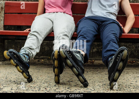 Menschen Freunde im Trainingsanzug mit Rollschuhen. Frau und Mann auf Bank im Freien entspannen. Stockfoto