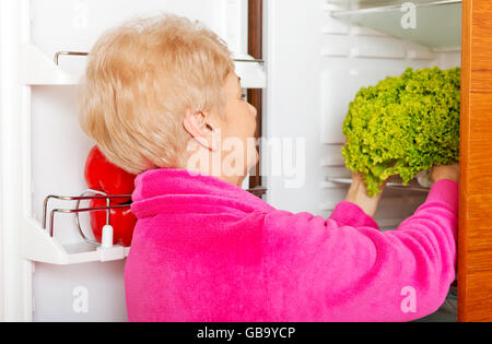 Ältere Frau, die einen grünen Salat aus Kühlschrank Stockfoto