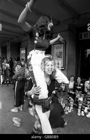 Gute Laune von zwei Fans der Bay City Rollers, als sie mit anderen Fans darauf warten, dass sich die Türen im Odeon, Hammersmith, für das erste von zwei Konzerten der Gruppe öffnen. Stockfoto