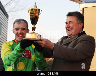 Der Jockey Ruby Walsh mit Trainer Paul Nicholls hebt die Siegertrophäe an, nachdem er mit Kauto Star im Stan James King George VI Chase während des Stan James Christmas Festivals auf der Kempton Racecourse den Sieg errungen hat. Stockfoto