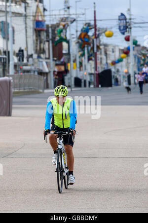 Mann in leuchtenden Weste und Helm, sein Fahrrad entlang der Promenade in Blackpool, Lancashire, UK Stockfoto
