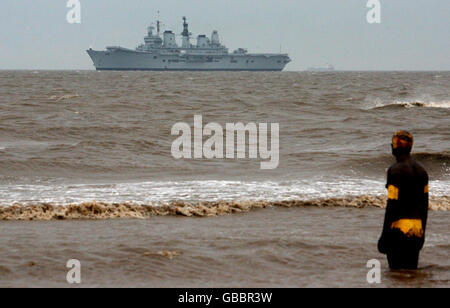 HMS Ark Royal geht an den Gormley Statuen in Crosby Beach, Merseyside vorbei, bevor sie in Liverpool anlegt. Stockfoto