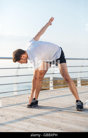 Ernster junger Mann Athlet Aufwärmen und Übungen am pier Stockfoto