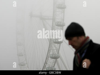 Ein Fußgänger auf der Westminster Bridge, wie das London Eye, am Southbank der Themse, ist in Nebel gehüllt. Stockfoto