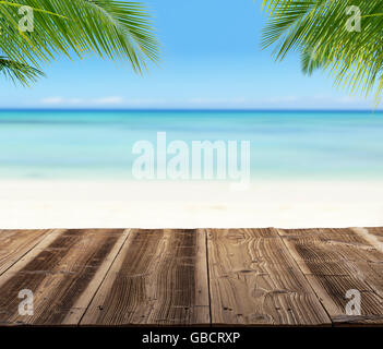 Leere Holzbohlen mit Strand im Hintergrund verwischen, einsetzbar für Product Placement, Palmblättern im Vordergrund Stockfoto