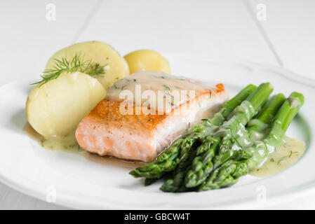 Nahaufnahme von gegrilltes Lachsfilet mit Kartoffeln und Spargel garniert mit Dillsauce auf weiße Platte angeordnet Stockfoto