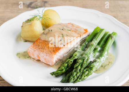 Nahaufnahme von gegrilltes Lachsfilet mit Kartoffeln und Spargel garniert mit Dillsauce auf weiße Platte angeordnet Stockfoto