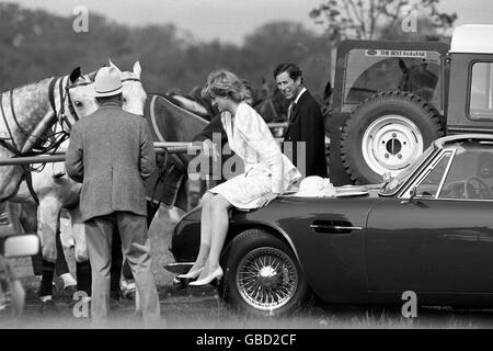 Die Prinzessin von Wales zieht ihren Ascot-Hut aus und ruht sich auf der Motorhaube des Aston Martin-Autos ihres Mannes bei einem Polospiel in Smith's Lawn, Windsor, aus. Der Prinz teilt dabei einen Witz. Stockfoto