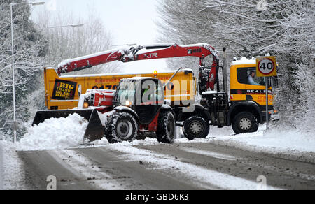 Ein Schneepflug ebnet den Weg für einen Lastwagen, der nach starkem Schneefall über Nacht auf einer Straße in Ingatestone, Essex, festsitzt. Stockfoto