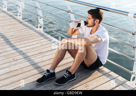 Attraktive junge Sportler sitzen auf Pier und Trinkwasser Stockfoto