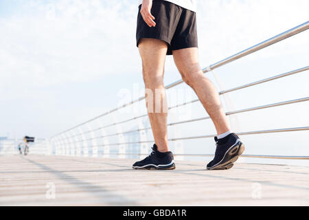 Nahaufnahme der junge Mann Beine in schwarzen Hosen und Turnschuhe zu Fuß auf Holzterrasse Stockfoto