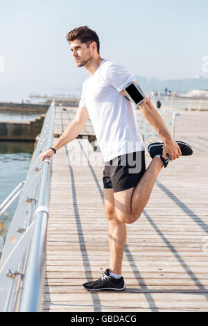 Hübscher Junge Sportler, die Dehnung der Beine während des Trainings am pier Stockfoto