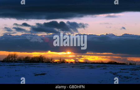 Die Sonne geht über schneebedeckten Feldern in der Nähe von Wotton-under-Edge, Gloucestershire, unter. Stockfoto