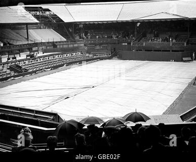 Tennis - Wimbledon Championships. Das Center Court ist bedeckt, wenn Regen auf den All England Club fällt (Bombenschäden aus dem Zweiten Weltkrieg sind in der linken oberen Ecke noch gut sichtbar) Stockfoto