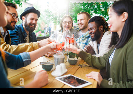 Glücklich interkulturelle freundliche junge Leute Toasten mit Getränken im Sommer-café Stockfoto