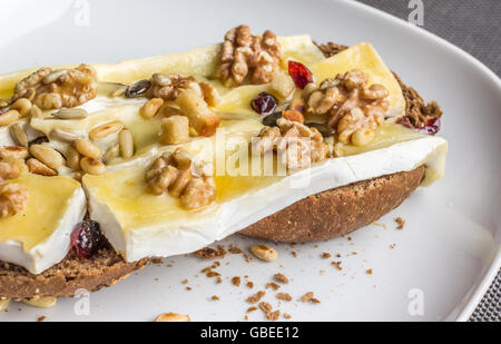 Geschmolzenem Brie mit Honig, Pinienkernen und Walnüssen auf Schwarzbrot Stockfoto