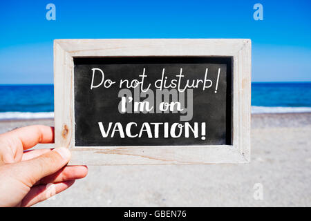 die Hand eines jungen Mannes mit einer Tafel mit dem Text nicht stören ich bin im Urlaub geschrieben, am Strand, mit der Stockfoto