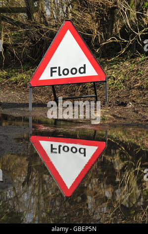 Allgemeine Ansicht eines Hochwasserwarnschildes neben Eine große Überschwemmung auf einer kleinen B-Straße Stockfoto