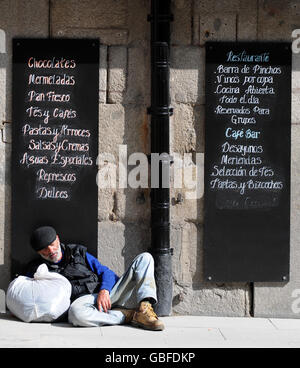 Ein Obdachloser schläft neben einer Tafel, auf der Lebensmittel in einem Café nebenan in Madrid, Spanien, angezeigt werden Stockfoto