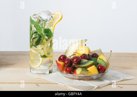 Scheiben von Obst, süßen Kirschen und Zitronen-Drink mit Eis in einem Glas auf Oberfläche aus Holzbrettern Stockfoto