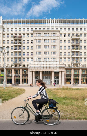 Radfahrer fährt vorbei an historischen sozialistischen ehemaligen DDR Mehrfamilienhäuser auf der Karl-Marx-Allee in Berlin Deutschland Stockfoto