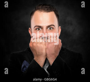Aufgeregt oder ängstlich junger Mann auf einem dunklen Hintergrund. Stockfoto