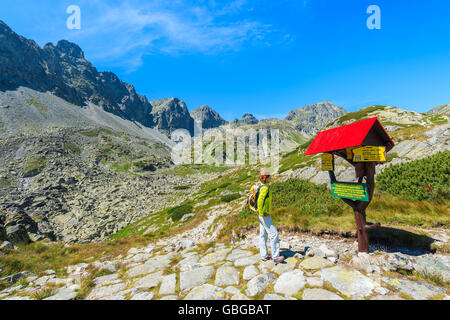 Junge Frau touristischen Blick auf Zeichen mit Spaziergang Zeit Entfernungen und Richtungen im Starolesna-Tal, hohe Tatra Mountains National Stockfoto