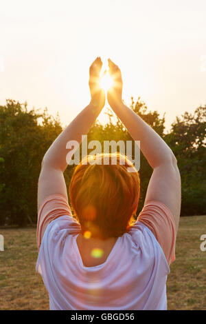 Ältere Frau macht eine Yoga-Meditation mit der Sonne in der Mitte ihrer Hände trainieren Stockfoto