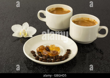 Milchkaffee Tassen und weiße Orchidee auf dem schwarzen Hintergrund. Tasse Kaffee. Kaffee-Pause. Kaffee am Morgen. Kaffee-Obertasse Stockfoto