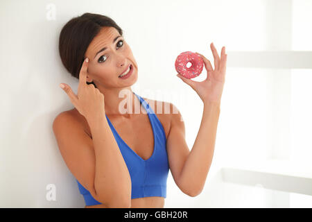 Junge Frau bei der Ausübung Kleidung wählen wenn zuckerhaltigen Essen beim Betrachten Sie Stockfoto