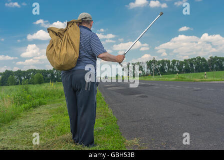 Senior woman Sack stehend auf einem am Straßenrand halten Walking stick Stockfoto
