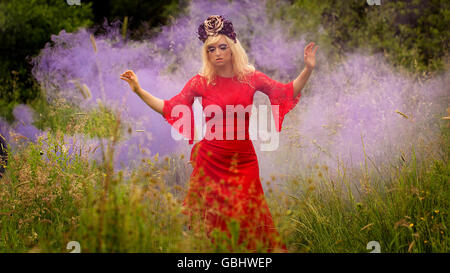 Blonde romantische Fee Elfe Modell in Wiese mit mit gold lila rose Krone Kopfschmuck, kontemplativen, lila Rauch Stockfoto