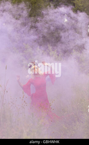 Blonde romantische Fee Elfe Modell in Wiese mit mit gold lila rose Krone Kopfschmuck, kontemplativen, lila Rauch Stockfoto