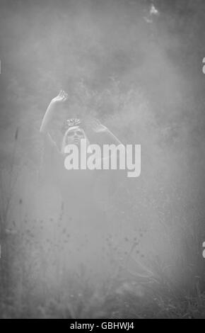 Blonde romantische Fee Elfe Modell in Wiese mit mit gold lila rose Krone Kopfschmuck, kontemplativen, Monochrom, Rauch Stockfoto