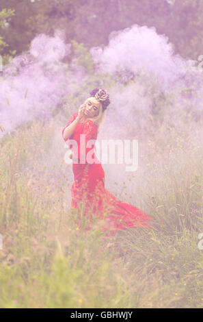 Blonde romantische Fee Elfe Modell in Wiese mit mit gold lila rose Krone Kopfschmuck, kontemplativen, lila Rauch Stockfoto