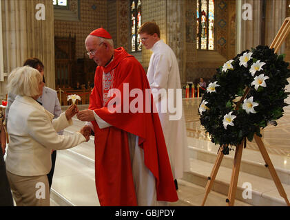 Kardinal Sean Brady hält eine Palmsonntagsmesse für die Angehörigen der Verschwundenen in der St. Patrick's Cathedral in Armagh, Nordirland, während Mary O'Neill, Schwester von Danny McIlhone, deren Überreste im November 2008 gefunden wurden, eine Lilie zum Gedenken an ihren Bruder von Kardinal Brady erhält. Stockfoto