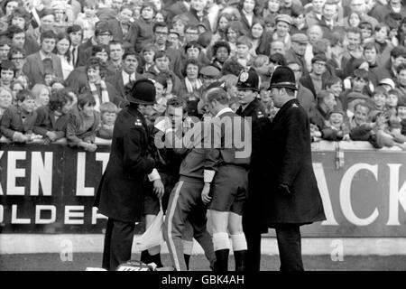 Schiedsrichter Ray Tinkler (r) sieht sich an, wie Linienmann Colin Carthlich (l), umgeben von Polizisten zum Schutz, von Leeds United Trainer Les Cocker (c) behandelt wird, nachdem er bei der Pitch-Invasion, die dem umstrittenen zweiten Tor von West Bromwich Albion folgte, verletzt wurde Stockfoto